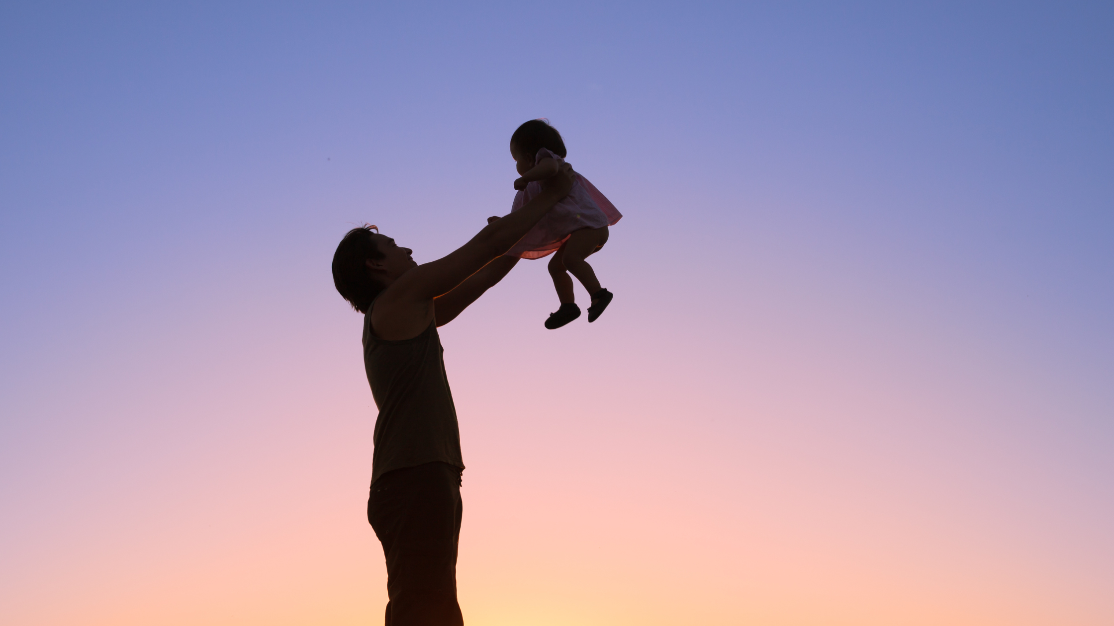 parent holding up their child behind a sunset.